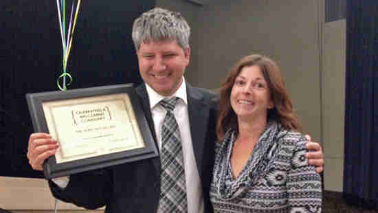 Michael receiving an award for helping create welcoming communities. He is standing with Anita Holland, and both are smiling. 