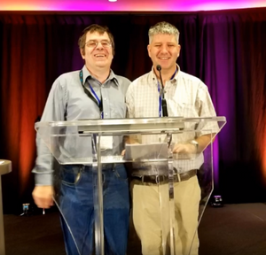 Michael standing side by side and smiling with fellow self-advocate David Johnston as they give a presentation. 