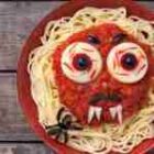Permalink to Halloween Spaghetti Monster Recipe A plate of spaghetti with a tomato sauce face, featuring egg eyes and black olive pupils. It has a jagged mouth with cheese teeth and black eyebrows, resembling a monster. Theres also a small plastic spider beside the face.