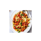 Permalink to Roasted Cherry Tomato Pasta A white plate of spaghetti is topped with colorful cherry tomatoes, green basil leaves, and a light sauce. A metal spoon rests beside the pasta.