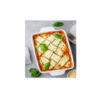 Permalink to Zucchini Lasagna (Not Watery!) Baked zucchini lasagna in a white square dish on a gray surface, topped with melted cheese and basil leaves. A plate with a fork and knife, some grated cheese, and a striped cloth are nearby.
