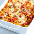 Permalink to Spring Vegetable Lasagna A white baking dish filled with baked zucchini casserole. The dish features visible layers of melted cheese, zucchini, diced tomatoes, and herbs, all baked to a golden-brown finish. The background is a marble countertop.