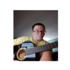 Person with short hair and glasses holding a black acoustic guitar. The background is indoors with soft lighting. The person is wearing a yellow shirt and looking towards the camera.