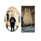 Permalink to Employment Award by Marcus Iregui A person stands in front of a lit Christmas tree holding two awards. Next to them is a close-up of a glass award that reads, 7 Years of Service presented to Marcus Ingul in recognition for hard work and service, January 2022, TileTown.